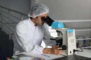 person in a medical suit uses a microscope